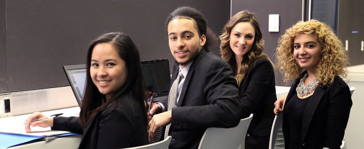 Four business students taking a break from working to pose for a photo. All professionally dressed and smiling.